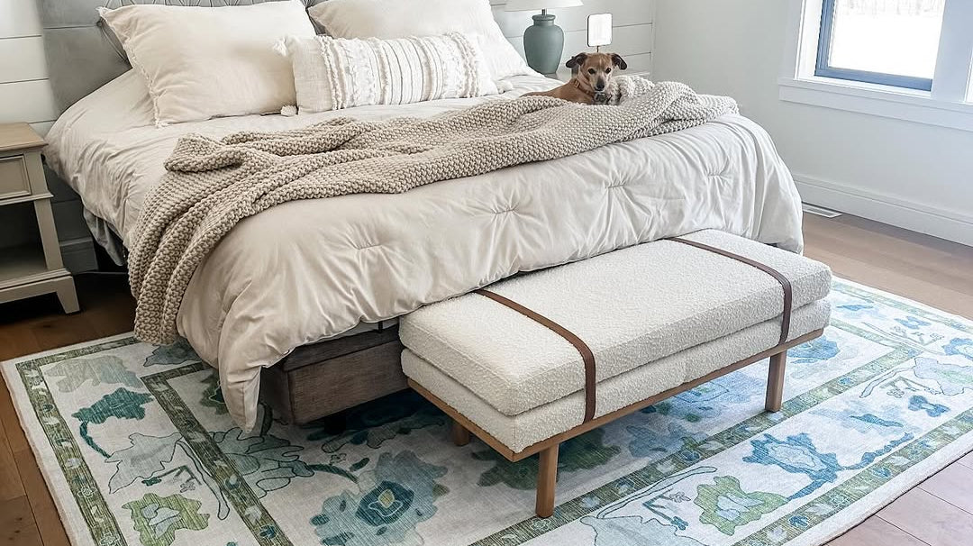 Blue and green Oushak rug in a neutral bedroom with beige furniture and cream walls