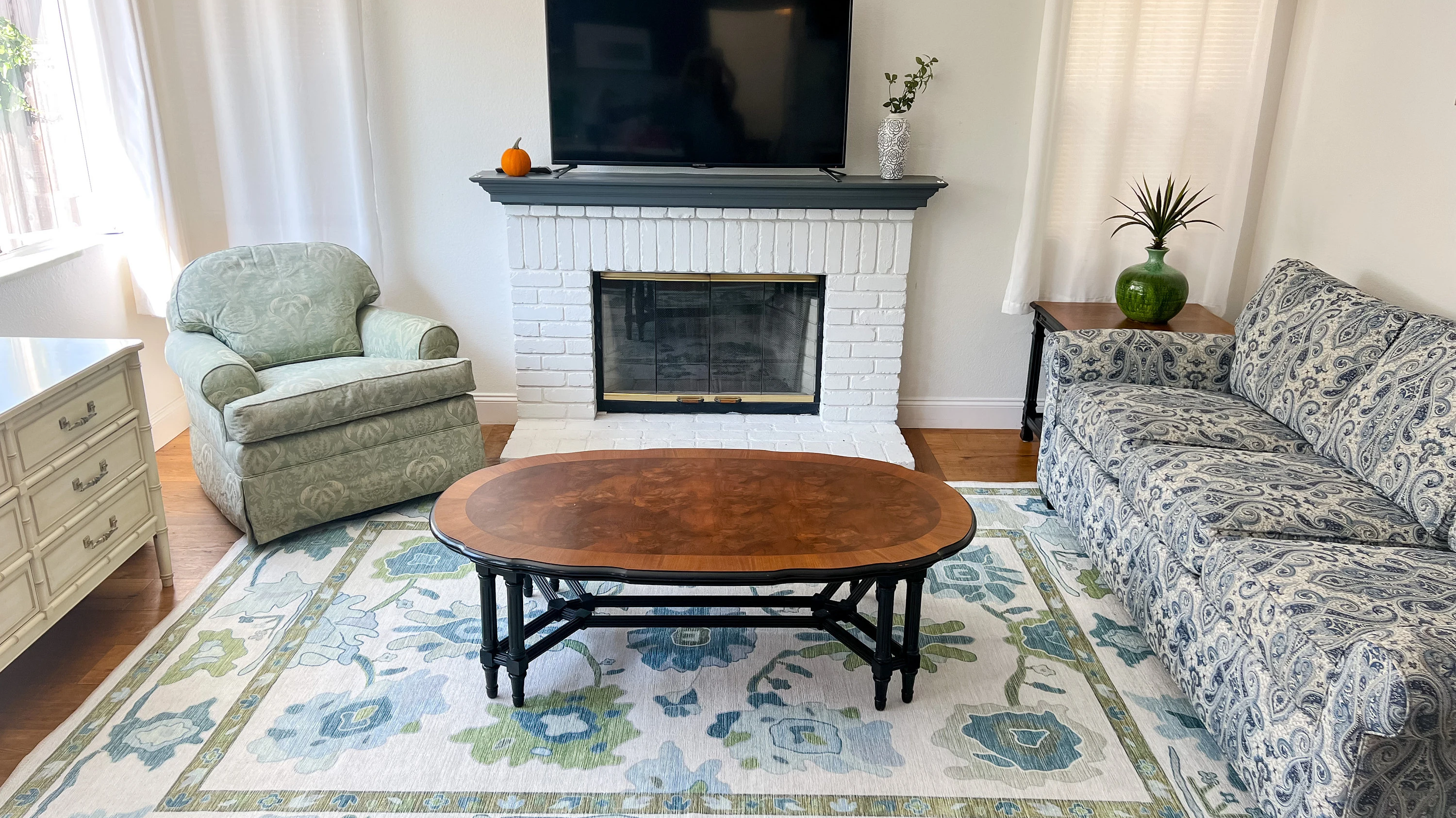 Living room with a green and blue floral area rug demonstrating correct rug size and furniture placement.