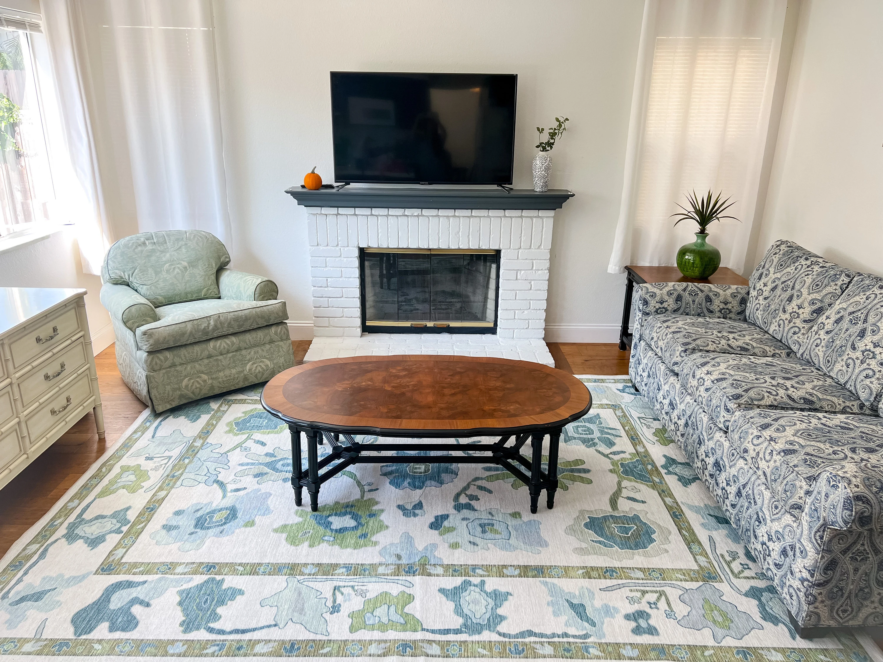 Living room with a green and blue floral area rug demonstrating correct rug size and furniture placement.