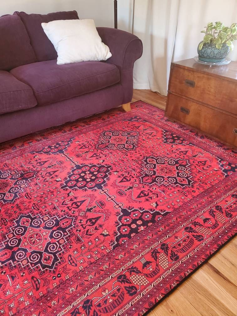 Red patterned rug in a living room with a purple couch and wooden dresser.