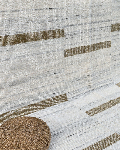 Cecilia wool kilim rug with mustard stripes next to a round woven basket