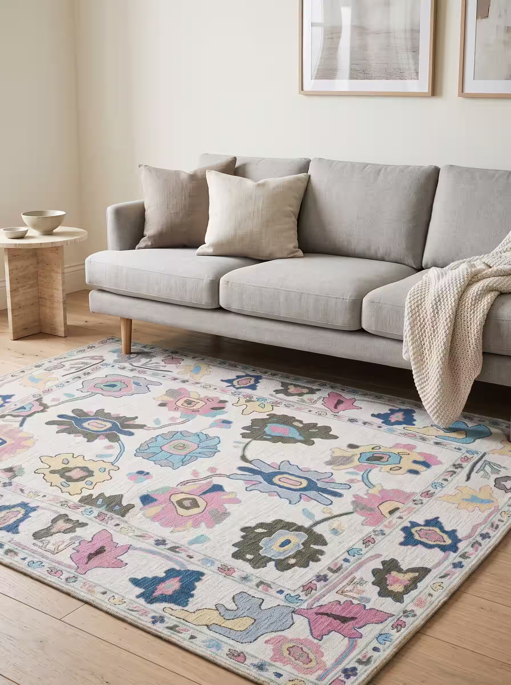 Cream Oushak area rug with blue and pink motifs paired with a light grey sofa in a modern living room