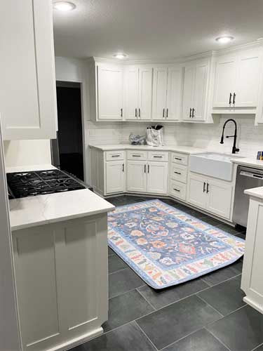 Modern kitchen with white cabinets, gray tiled floor, and a decorative rug. Kitchen Rugs - Fame Rugs.