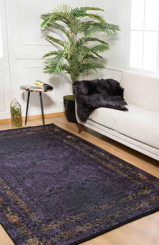 Living room with a dark patterned rug, white sofa, and potted plant. Marble Rugs - Fame Rugs.